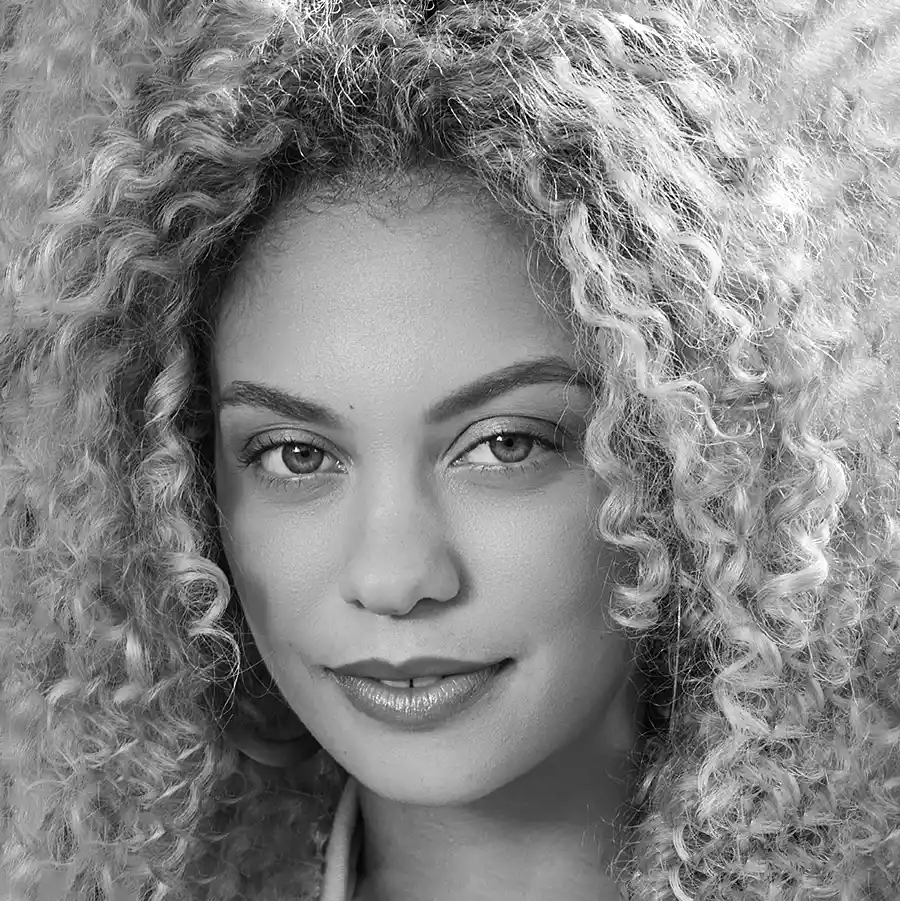 A female presenting person with curley hair and clear skin looking at the camera