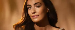 Close-up of a woman with glowing skin and dark hair looking toward the camera against a warm, golden background.