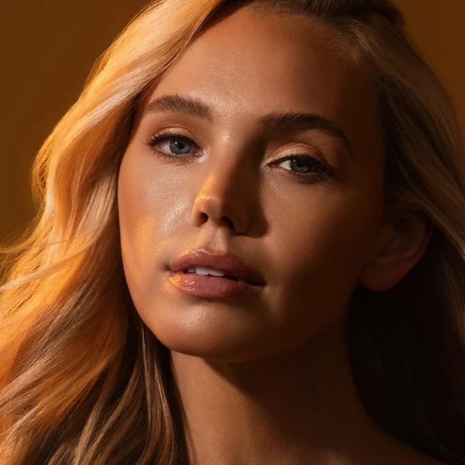 Female model standing in illuminated light with a relaxed, confident pose, highlighting smooth, radiant skin in a modern tanning and wellness environment.