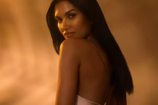 Portrait of a woman with long dark hair looking over her shoulder against a warm, golden lit background.