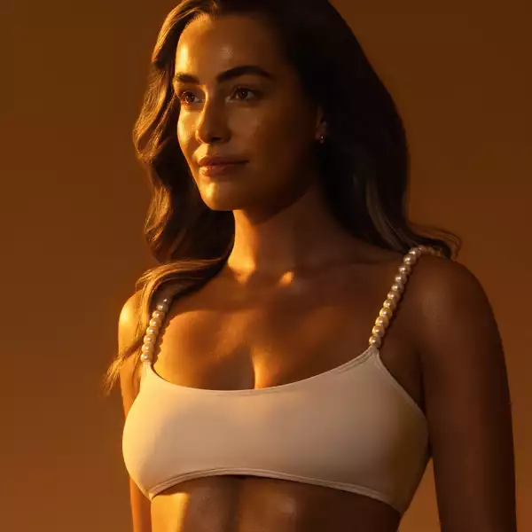 Female model standing in soft, illuminated light with a confident pose, highlighting smooth, glowing skin in a modern tanning and wellness salon setting.