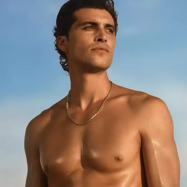 Male model standing outdoors in natural light with a confident pose, showcasing a healthy, sun-kissed appearance in a lifestyle setting.