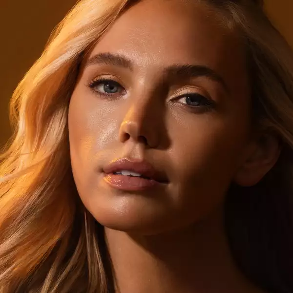 Female model standing in illuminated light with a relaxed, confident pose, highlighting smooth, radiant skin in a modern tanning and wellness environment.