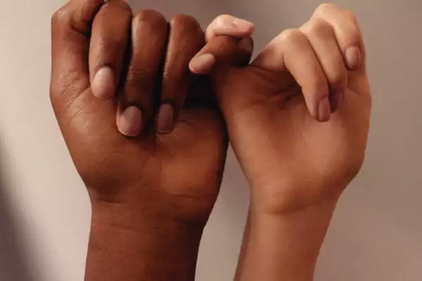 Two hand of different skin tones link pinkies.