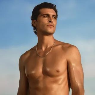 Shirtless man with dark hair looking off into the distance against a blue sky.