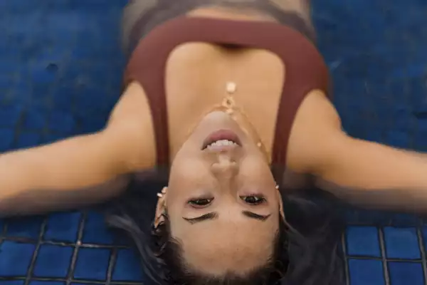 A woman in a burgundy bikini lays on her back and stares into the camera from a set of pool steps